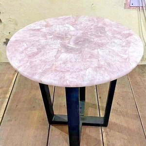 May include: A round pink table with a black metal base. The table top is made of natural stone with a unique pattern.