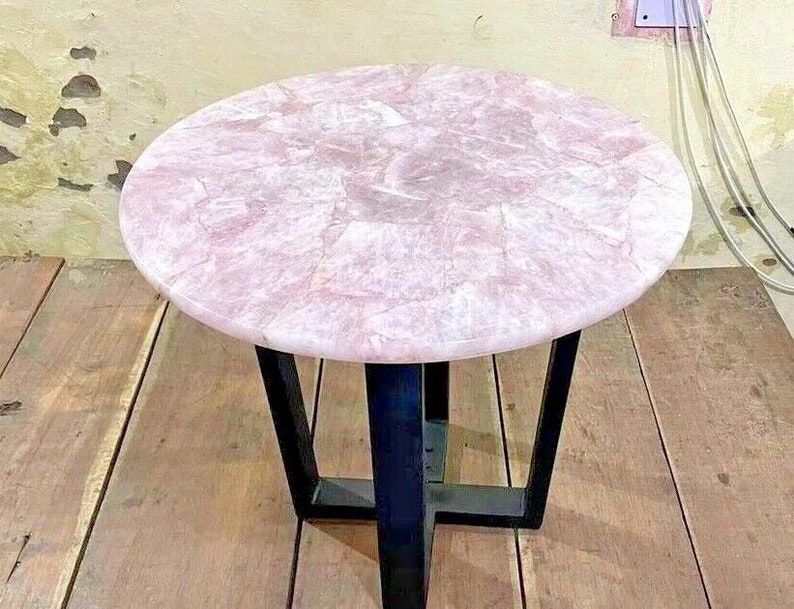 May include: A round pink table with a black metal base. The table top is made of natural stone with a unique pattern.