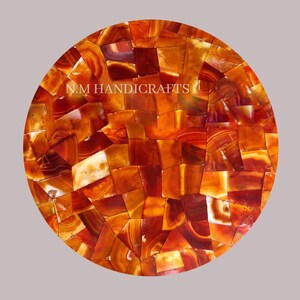 May include: Round table top made of red agate stone. The top is made of many small pieces of agate that are arranged in a mosaic pattern. The agate is a natural stone with a variety of colors and patterns. The table top is perfect for a coffee table or end table. N.M. HANDICRAFTS is printed on the table top.