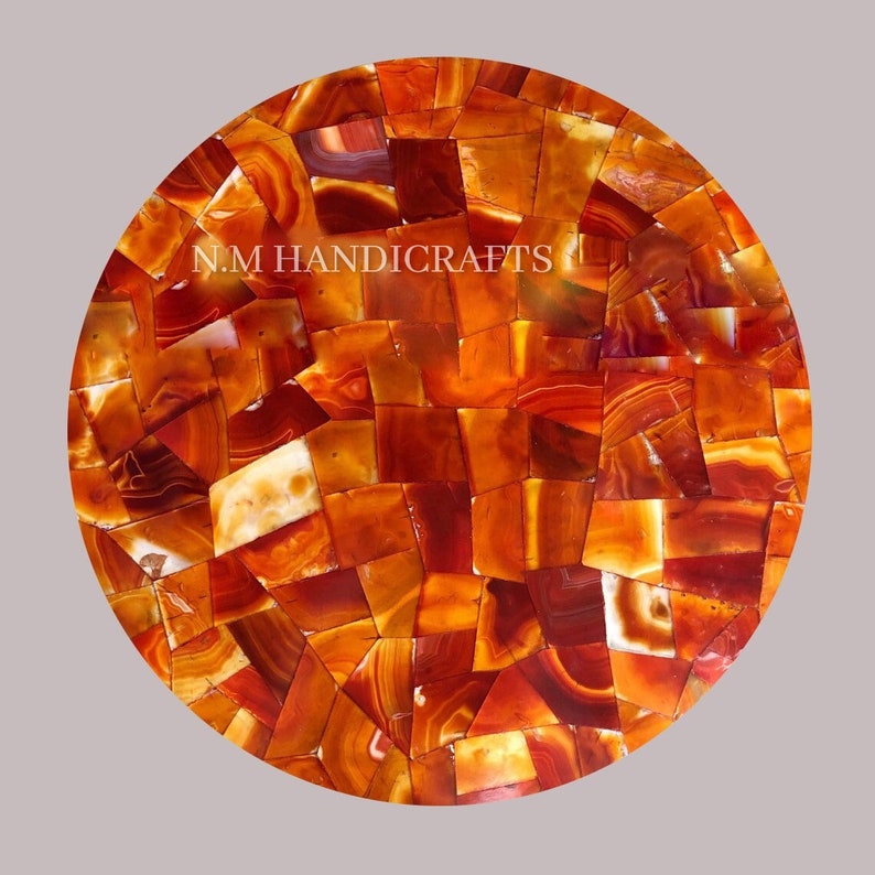 May include: Round table top made of red agate stone. The top is made of many small pieces of agate that are arranged in a mosaic pattern. The agate is a natural stone with a variety of colors and patterns. The table top is perfect for a coffee table or end table. N.M. HANDICRAFTS is printed on the table top.