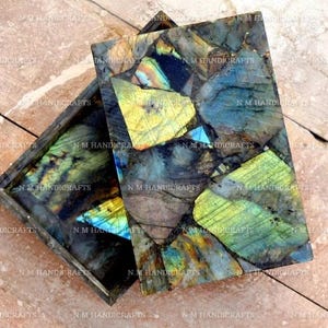 May include: A rectangular box made of labradorite stone. The box is made of many pieces of labradorite, each with a different pattern of iridescent blue, green, and gold.