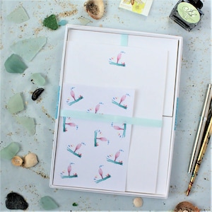 May include: A set of white stationery with a blue ribbon. The stationery features a repeating pattern of watercolour illustrations of pink and green seahorses. The stationery is packaged in a white box.