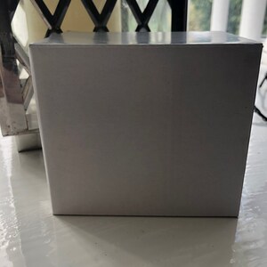 May include: A white rectangular box with a smooth, glossy surface. The box is sitting on a white surface.