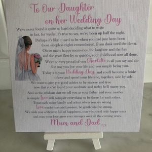 May include: A white card with a pink and purple design featuring a bride and groom illustration. The card reads "To Our Daughter on her Wedding Day" and includes a heartfelt message from the bride's parents. The card is signed "Mum and Dad".