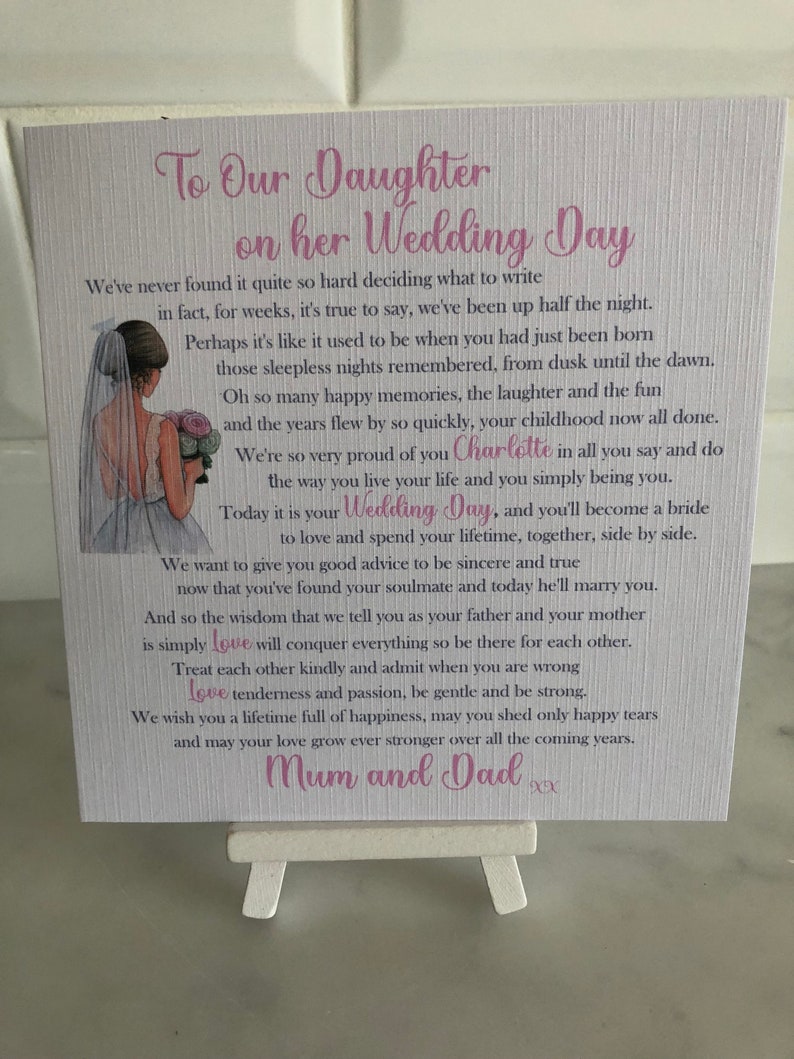 May include: A white card with a pink and purple design featuring a bride and groom illustration. The card reads "To Our Daughter on her Wedding Day" and includes a heartfelt message from the bride's parents. The card is signed "Mum and Dad".