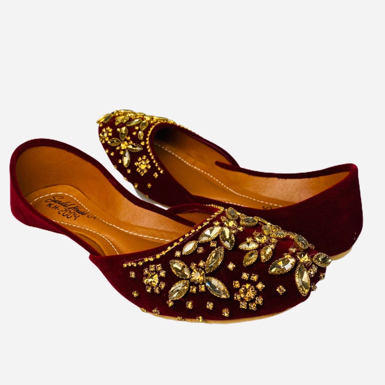 May include: A pair of maroon velvet shoes with gold and clear rhinestone embellishments. The shoes have a pointed toe and a low heel.