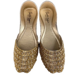 Puede incluir: Un par de zapatos planos dorados adornados con cuentas. Los zapatos tienen un acabado de brillo dorado y est&aacute;n decorados con peque&ntilde;as cuentas doradas. El interior de los zapatos est&aacute; etiquetado como "Sandal House, K.H. - 2000".