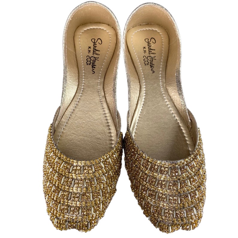 Puede incluir: Un par de zapatos planos dorados adornados con cuentas. Los zapatos tienen un acabado de brillo dorado y est&aacute;n decorados con peque&ntilde;as cuentas doradas. El interior de los zapatos est&aacute; etiquetado como "Sandal House, K.H. - 2000".