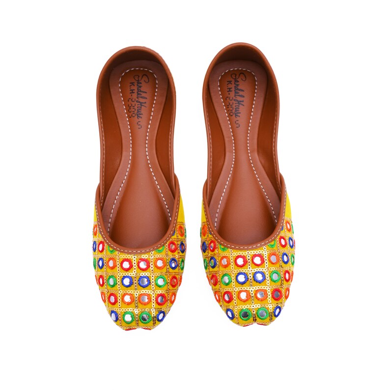 May include: A pair of yellow flat shoes with colorful mirror embellishments. The shoes have a brown leather insole with the text "Sandals House" and "KH-2303" printed on them.