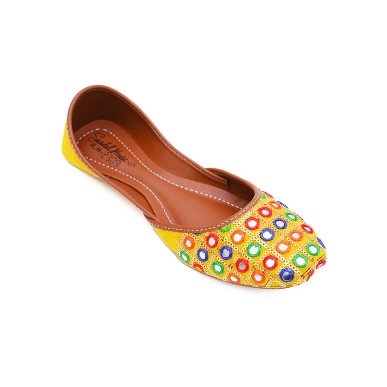 May include: Yellow embroidered flat shoes with colorful round mirror embellishments. The shoes have a brown leather insole and a pointed toe.