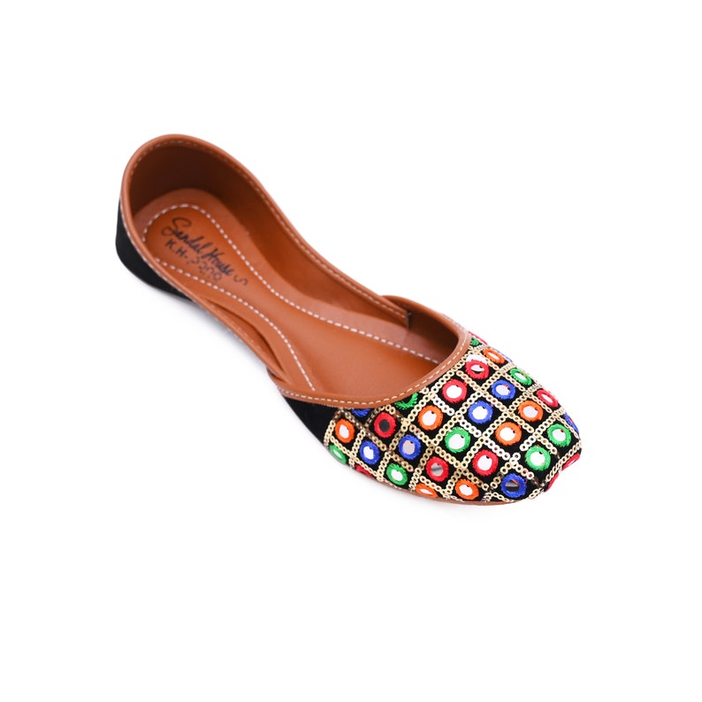 May include: Black embroidered flat shoes with colorful mirror work and gold sequins. The shoes have a brown leather insole and a pointed toe.