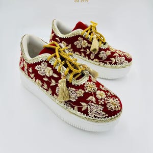 May include: Red sneakers with gold floral embroidery, white soles, and gold trim. The laces are adorned with gold tassels. The brand name "Sandal House" is displayed in the upper right corner of the image.