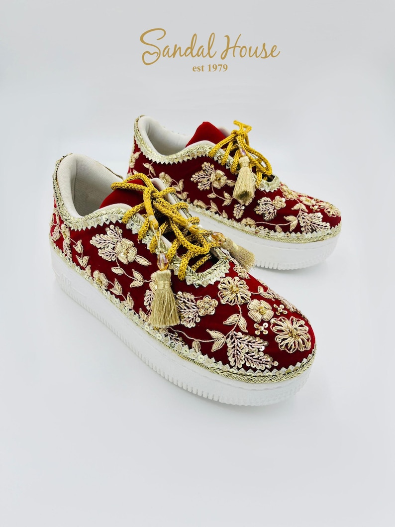 May include: Red sneakers with gold floral embroidery, white soles, and gold trim. The laces are adorned with gold tassels. The brand name "Sandal House" is displayed in the upper right corner of the image.