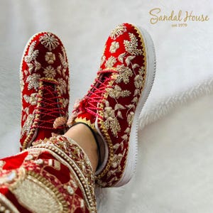 May include: Red sneakers with detailed gold floral embroidery. The shoes feature red laces and a white sole. The text "Sandal House est 1979" is in the upper right corner. The shoes are part of a set.