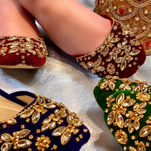 May include: Three pairs of embellished slippers in red, green, and blue velvet. Each slipper is decorated with gold and clear rhinestones.