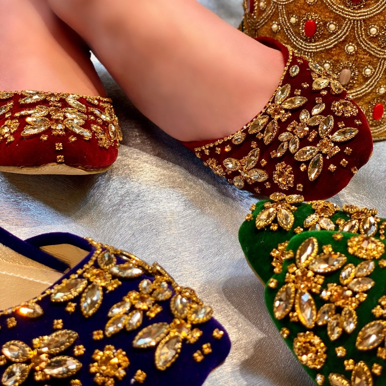 May include: Three pairs of embellished slippers in red, green, and blue velvet. Each slipper is decorated with gold and clear rhinestones.