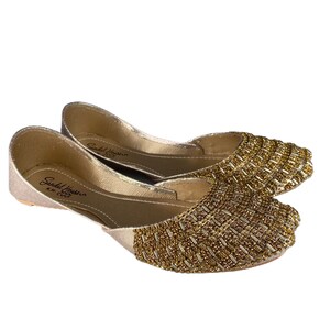 Puede incluir: Un par de zapatos planos dorados con un dise&ntilde;o de cuentas. Los zapatos tienen una punta puntiaguda y un tac&oacute;n bajo. El nombre de la marca "Sandal House" es visible en la plantilla.