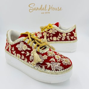 May include: Red sneakers with gold floral embroidery and white soles. The shoes feature gold laces with tassels and are trimmed with gold sequins. The brand name "Sandal House" is visible in gold script.
