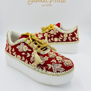 May include: Red sneakers with gold floral embroidery and tassels. The shoes have white soles and gold trim. The text "Sandal House est 1979" is in gold script above the shoes.