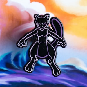 May include: Black and purple enamel pin featuring a cartoon silhouette of a Pokemon character, Mewtwo, with a menacing expression.