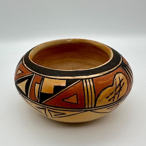May include: A hand-painted ceramic bowl with a geometric design in black, orange, and white on a tan background.