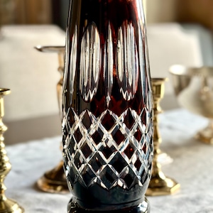 May include: A dark red crystal vase with a diamond pattern and a clear glass base.