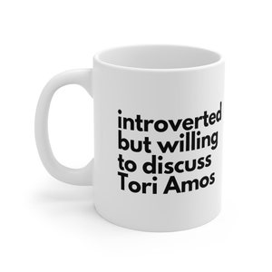 Könnte beinhalten: Weiße Keramik-Kaffeetasse mit schwarzem Text, der "introvertiert, aber bereit, Tori Amos zu diskutieren" lautet.