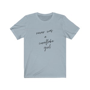May include: A light blue t-shirt with the text "never was a cornflake girl" printed in black.