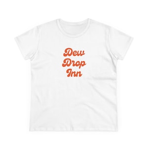 May include: White t-shirt with the text "Dew Drop Inn" in orange script. The shirt has a crew neck and short sleeves. The text is stacked vertically.
