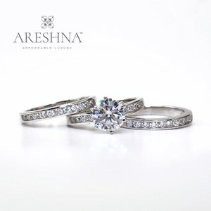Puede incluir: Un juego de anillos de compromiso de diamantes de tres piezas con una piedra central grande y dos anillos de banda m&aacute;s peque&ntilde;os. Los anillos son de metal blanco y tienen un dise&ntilde;o cl&aacute;sico.