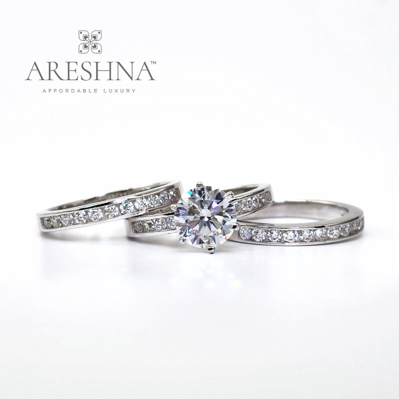 Puede incluir: Un juego de anillos de compromiso de diamantes de tres piezas con una piedra central grande y dos anillos de banda m&aacute;s peque&ntilde;os. Los anillos son de metal blanco y tienen un dise&ntilde;o cl&aacute;sico.