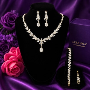 Areshna™ The Aurora luxury 18K gold bridal jewelry set featuring Swarovski crystals and Diamonash™ lab-created diamond simulants, displayed with a matching necklace, earrings, bracelet, and signature royal purple box on satin.