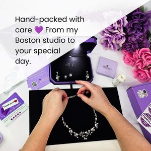 Behind-the-scenes view of hands carefully packing a luxury bridal and gala jewelry set by Areshna™ inside a signature purple LED lighted gift box at a Boston studio. This flat-lay image highlights artisanal care, custom packaging, thank-you cards, and floral accents, emphasizing handcrafted quality and personalized small-business service for special occasions and luxury gifts.
