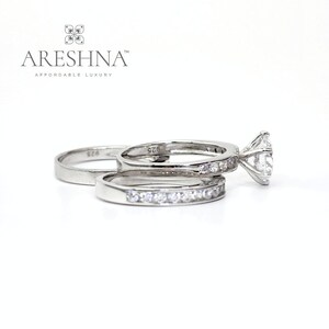Puede incluir: Un juego de anillos de compromiso de plata con una piedra central redonda grande y una banda m&aacute;s peque&ntilde;a con piedras engastadas en pav&eacute;. Los anillos est&aacute;n estampados con "925" en el interior.