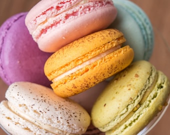 Puede incluir: Primer plano de una pila de macarons coloridos. Los macarons están dispuestos en un cuenco de vidrio. Los macarons son de varios colores, incluyendo rosa, amarillo, verde y morado.