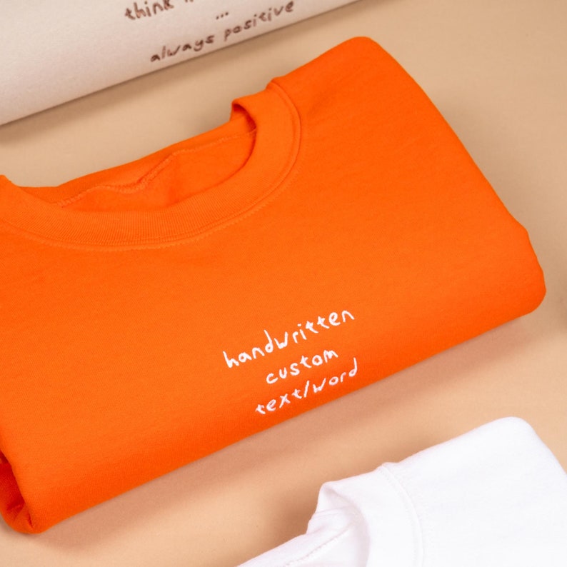 Orange vibrant winter jumper displaying custom embroidered text on the front chest