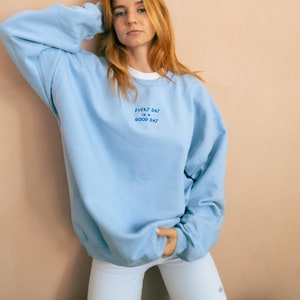 A woman wearing oversized sky blue sweatshirt at home with Royal blue thread embroidery