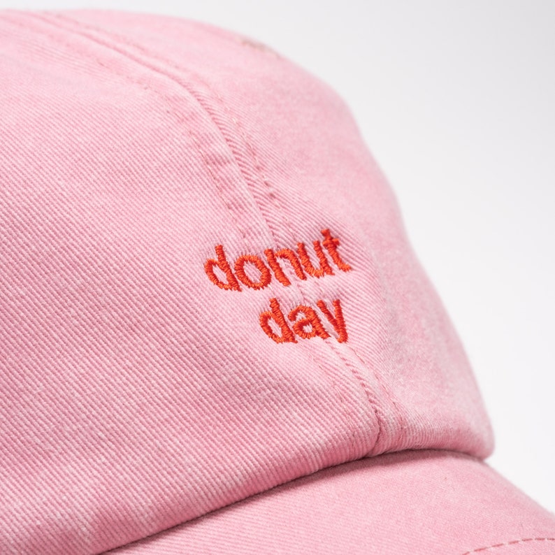 Close up of red thread embroidery on the front of a pink cap saying donut day