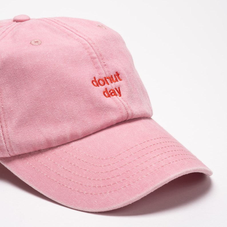 A six panel unstructured washed out cap in pink colour with red embroidered text donut day