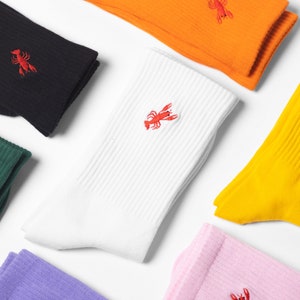 Peut inclure: Un ensemble de chaussettes colorées avec un motif de homard brodé en rouge. Les chaussettes sont de différentes couleurs, notamment noir, blanc, jaune, rose et violet.