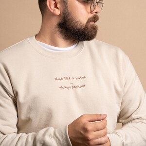 Man wearing a sand colour sweatshirt with custom text embroidered on the chest