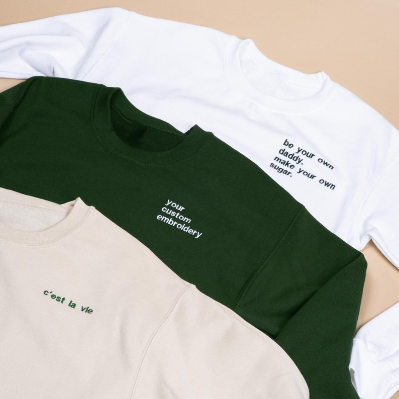 White green and sand coloured sweatshirts flat layer displaying custom embroidered text on left chest side