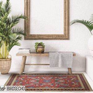May include: A red, blue, and green patterned rug with a beige border. The rug is placed in front of a wooden bench with a gray throw blanket on top. A potted plant sits on the bench.