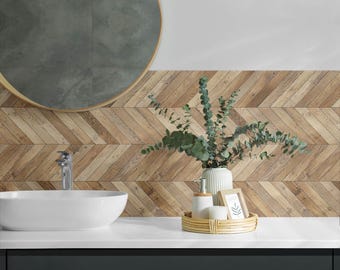 May include: A white ceramic sink with a chrome faucet sits on a white countertop. Behind the sink is a wall with a wood-look herringbone tile pattern. A wooden tray with a vase of green eucalyptus branches, a white bottle with a pump, and a white candle sits on the countertop.