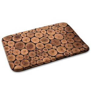 Op de afbeelding: Een bruine en zwarte badmat met een houtnerfpatroon van boomringen. De mat is gemaakt van een zacht, absorberend materiaal en is perfect om een ​​rustieke touch aan uw badkamer toe te voegen.