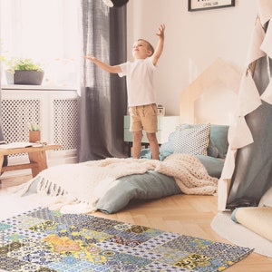 May include: A yellow, blue, and white patterned rug with a patchwork design. A child is playing with a black ball in a room with a bed and a teepee.