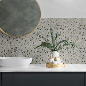 Op de afbeelding: Een moderne badkamer met een wit aanrecht, een wastafel en een donkerblauwe kast. Een ronde spiegel hangt erboven en de muur heeft een botanisch behangontwerp met groene en grijze bladeren. Een geweven dienblad bevat zeep, een dispenser en een kleine ingelijste foto.