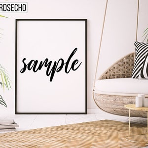 Puede incluir: Un póster enmarcado en negro con la palabra "sample" escrita en cursiva blanca sobre un fondo blanco. El póster está colgado en una pared blanca en una habitación con una silla colgante de mimbre y una mesa pequeña.