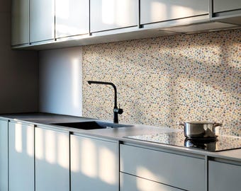 May include: A modern kitchen with gray cabinets and a backsplash made of small, colorful pebbles. A black faucet is mounted above a stainless steel sink. A black stovetop is visible in the foreground.