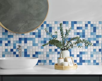May include: A white bathroom sink with a blue and white mosaic tile backsplash. A vase with green leaves and a small wooden tray with decorative items are on the counter.
